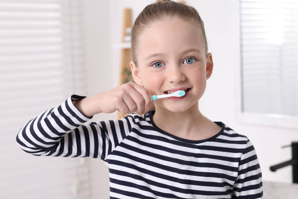 Cute little girl brushing her teeth with plastic toothbrush in bathroom - Foto, afbeelding