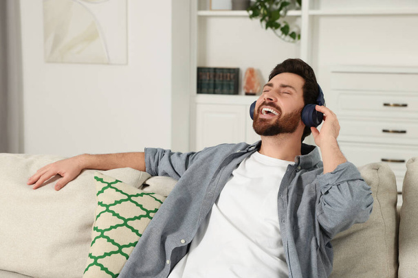 Happy man listening music with headphones on sofa indoors - Fotoğraf, Görsel
