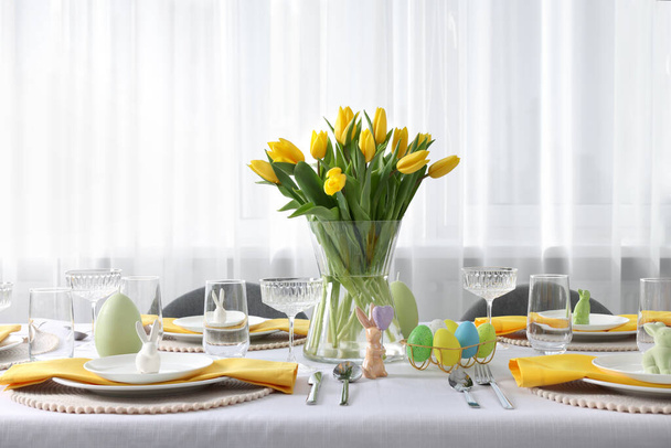 Festive table setting with glasses, painted eggs and vase of tulips. Easter celebration - Foto, afbeelding