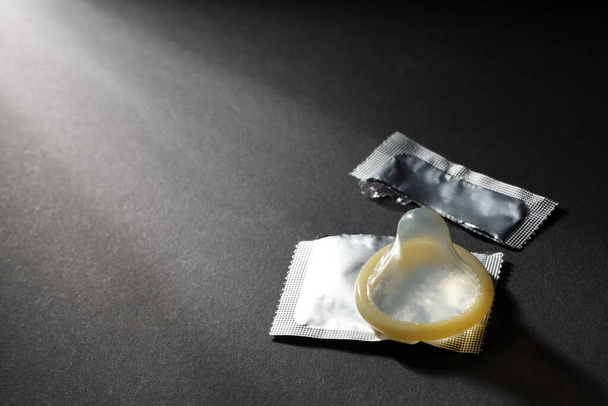 Unpacked condom and torn package on black background, space for text. Safe sex - Foto, afbeelding