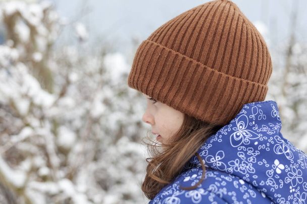 Portrét krásné dívky v pleteném klobouku na pozadí zimního lesa - Fotografie, Obrázek