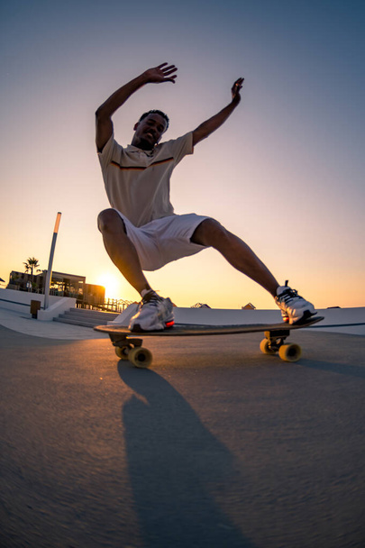 Surf skater training surfing moves near the beach at sunset. - Valokuva, kuva