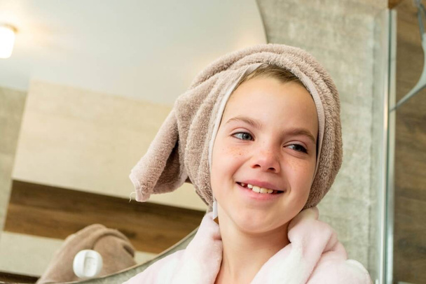 Entspannte junge Mädchen Modell trägt Handtuch auf dem Kopf gewickelt, fühlt sich nach dem Duschen erfrischt, hat gesunde saubere weiche Haut, posiert im gemütlichen Badezimmer. Mädchen, Schönheit und Hygienekonzept. Hochwertiges Foto - Foto, Bild
