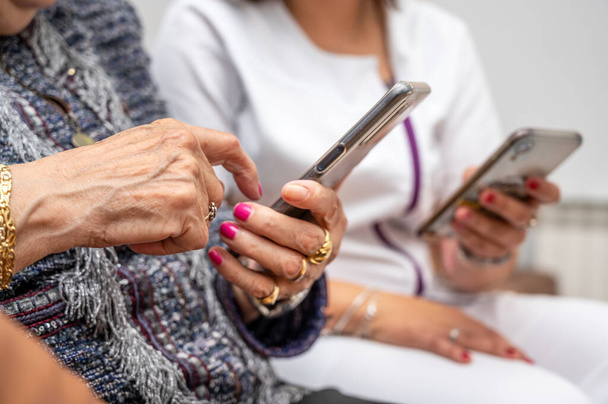 Verpleegster leren oudere vrouw hoe je mobiele telefoon te gebruiken, senior grootmoeder leren om smartphone te gebruiken in het verpleeghuis. Moderne technologie voor ouderen. Hoge kwaliteit foto. - Foto, afbeelding