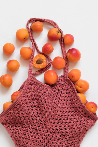Crochet burgundy shopping bag with fresh organic apricots on a white background. Healthy eating concept. - Fotografie, Obrázek