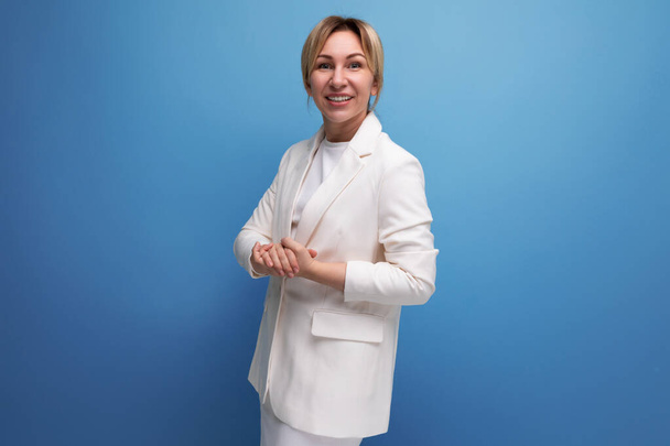 νεαρή λεπτή ξανθιά επιχειρηματίας σε ένα λευκό κομψό σακάκι και φούστα σε μπλε φόντο με αντίγραφο χώρο. - Φωτογραφία, εικόνα
