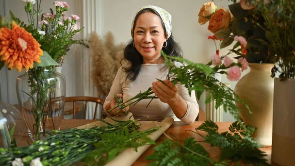 Позитивний середнього віку жіночий флорист готує букет за столом у квітковому магазині. Флористика та концепція малого бізнесу
. - Фото, зображення
