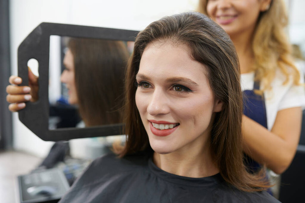 Smiling young brunette having her hair done in beauty salon - Photo, Image