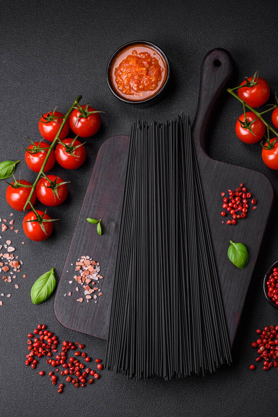 Massa de espaguete preta crua com tomate, sal, especiarias e ervas em um fundo de concreto escuro - Foto, Imagem