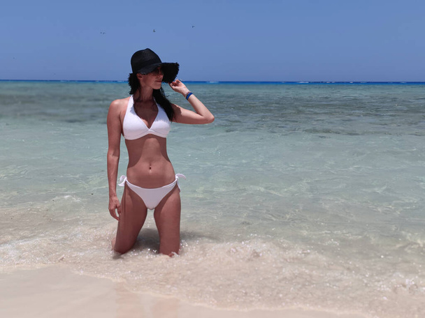 Slim brunette girl, woman on the beach in bikini with sunglasses - Фото, изображение