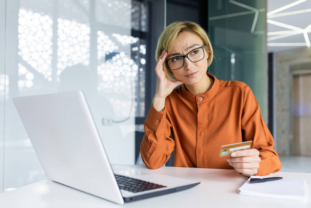 Sad and unhappy woman inside workplace office with laptop holding bank credit card, businesswoman cheated got negative account balance and online money transfer error. - Foto, Bild