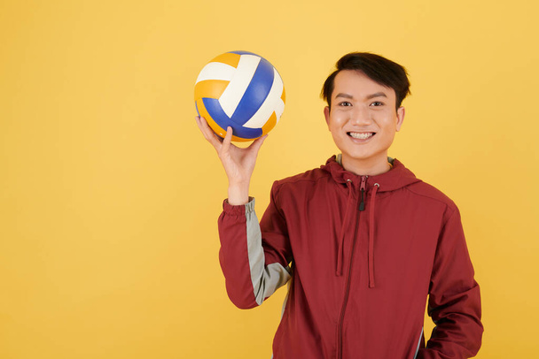 Sonriente joven vietnamita sosteniendo la pelota de voleibol, aislado en amarillo - Foto, imagen