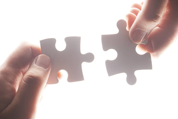 Puzzle, synergy and solution with hands of person on white background for achievement, goal and development. Mission, game and cooperation with jigsaw pieces for support, success and integration. - Photo, image