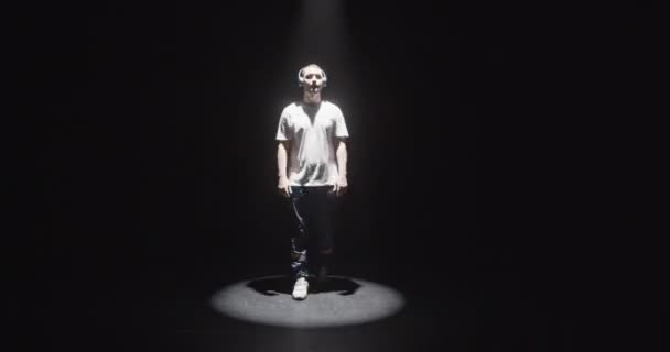 Real time full body of young male Caucasian dancer in headphones listening to nice song while coming out of darkness then dancing contemporary dance under spotlight making smooth movements - Filmagem, Vídeo