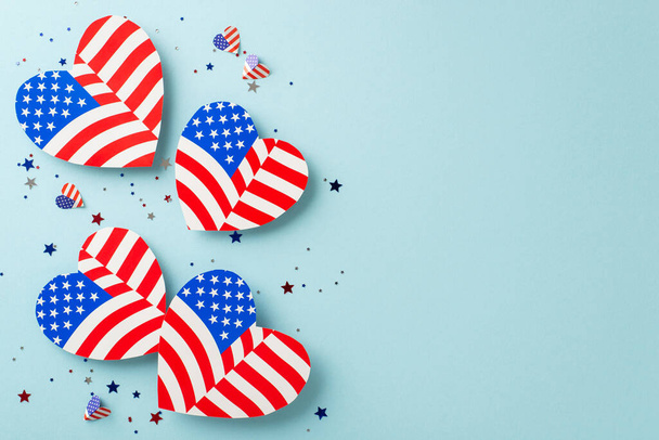 Freiheitsfeiern in den USA. Overhead-Aufnahme ikonischer Verzierungen: Herzen mit amerikanischem Flaggenmotiv, Konfetti, arrangiert auf pastellblauer Oberfläche mit Platz für Text oder Werbeinhalte - Foto, Bild