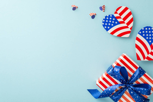 Flag Day festivities. Overhead shot of representative ornaments: hearts with American flag motif and themed giftbox, on a pastel blue background with an empty area for messages or advertising - Photo, Image