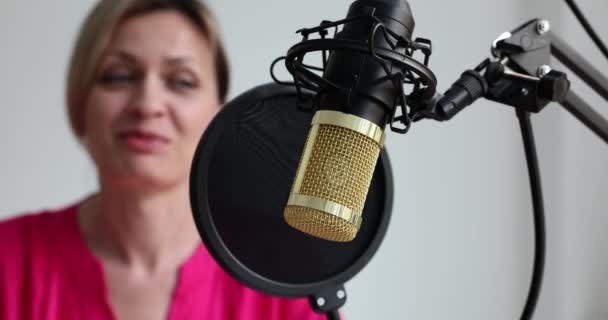 Γυναίκα podcaster κάθεται στο τραπέζι και μιλάει στο μικρόφωνο σε τρίποδο και μοιράζεται πληροφορίες. Κορίτσι κάνοντας podcast ήχου για το κοινό στο διαδίκτυο closeup - Πλάνα, βίντεο