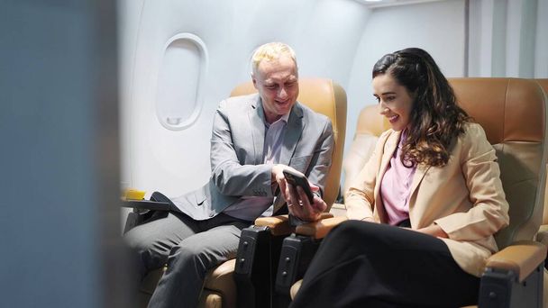 Deux voyageurs d'affaires assis à bord d'un avion qui regardent ensemble leur smartphone, vérifient leur e-mail ou leur plan de voyage d'affaires. Profitant d'un long vol d'affaires. Voyage d'affaires, concept technologique - Photo, image