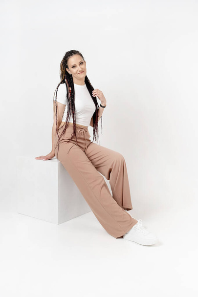 Fashionable young beautiful woman. Slim girl with dreadlocks in an active pose in a white pants and top. Fashion, clothing and style. - Fotoğraf, Görsel