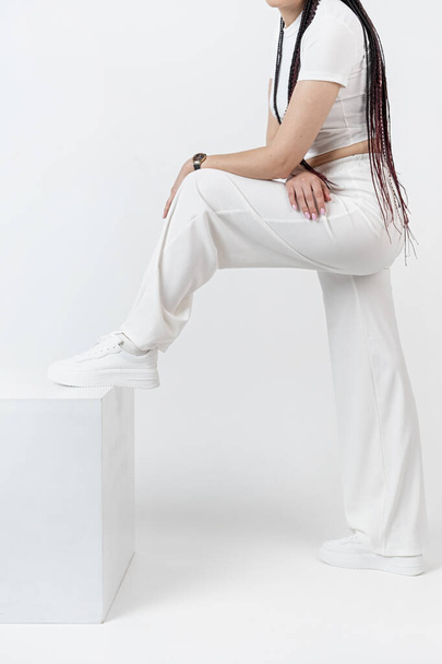 Joven mujer hermosa de moda. Chica delgada con rastas en una pose activa en un pantalón blanco y parte superior. Moda, ropa y estilo. - Foto, imagen