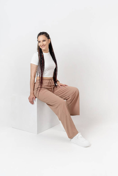 Fashionable young beautiful woman . Slim girl with dreadlocks in an active pose in a white pants and top . Fashion, clothing and style. - Photo, Image