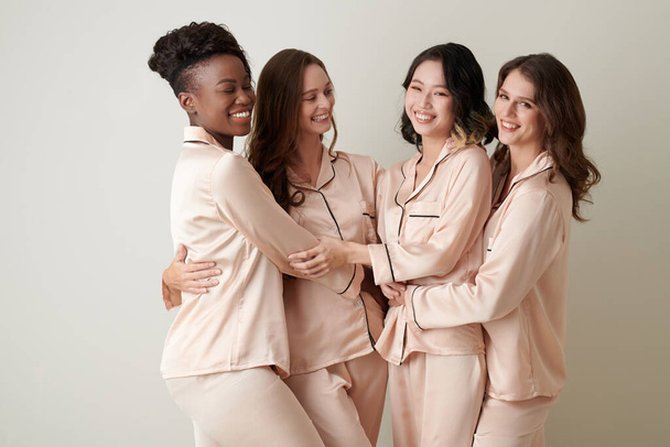 Rozmanitá skupina přítelkyň v hedvábném pyžamu se usmívá a objímají se - Fotografie, Obrázek