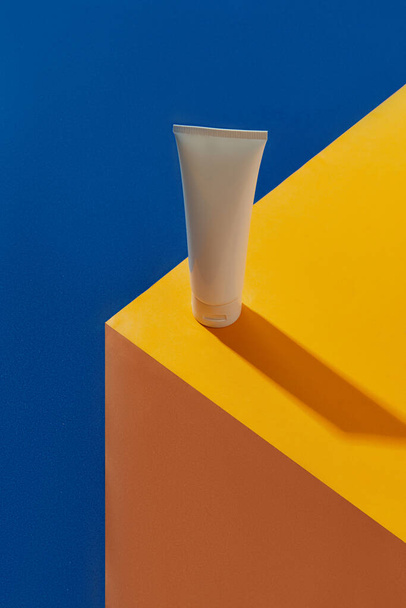 Top view blanco witte tube fles met huidverzorgingsproduct op blauwe en oranje creatieve achtergrond. Gezichtsbehandeling wellness concept. - Foto, afbeelding