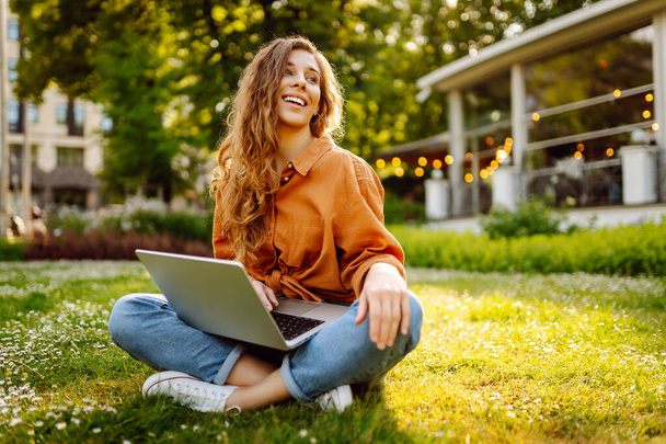 Mujer joven sonriente con una computadora portátil que trabaja o estudia al aire libre en línea. Concepto de educación, negocios, blog o freelance. - Foto, imagen