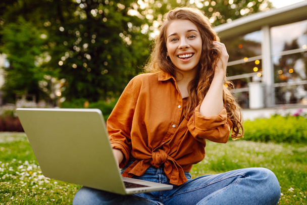 Smiling young woman with a laptop working or studying online outdoor. Concept for education, business, blog or freelance. - Valokuva, kuva