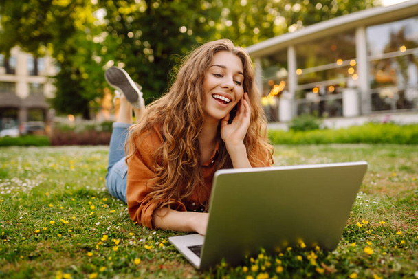 Smiling young woman with a laptop working or studying online outdoor. Concept for education, business, blog or freelance. - Fotó, kép
