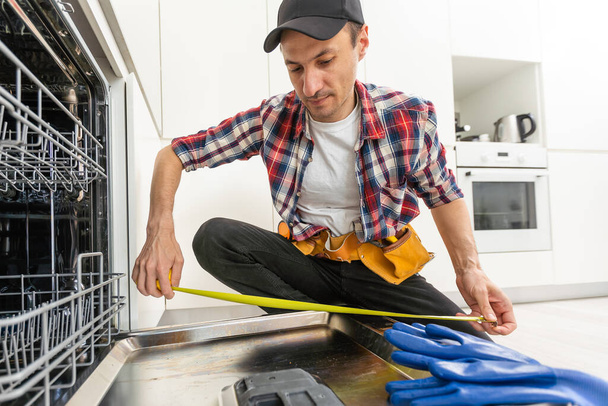 Worker using screwdriver to repair dishwasher at home stock photo. High quality photo - Valokuva, kuva