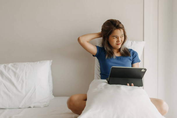 Asian woman works digital online on her bed feeling tired on vacation. - Zdjęcie, obraz