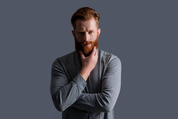 touch moustache and beard care. handsome unshaven guy has beard and moustache. unshaven guy with beard and moustache isolated on grey background. studio shot of unshaven guy. - Photo, Image