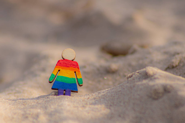 ЛГБТ деревянные люди на пляже на песке. Пара, стоящая на пляже с радужным флагом, равные права, символ ЛГБТ-сообщества. ЛГБТ-флаг на песчаном пляже. Концепция летнего путешествия. Символ однополых отношений - Фото, изображение