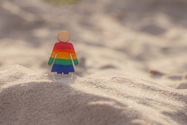 Des personnes LGBT en bois sur la plage sur le sable. Couple debout sur la plage avec drapeau arc-en-ciel, l'égalité des droits, symbole de la communauté LGBT. Drapeau LGBT sur une plage de sable fin. Concept de voyage d'été. Un symbole du même sexe - Photo, image