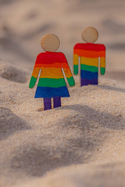 LGBT wooden people on the beach on the sand. Couple standing on beach with rainbow flag, equal rights, symbol of LGBT community. LGBT flag on a sandy beach. Summer travel concept. A symbol of same-sex - Photo, Image