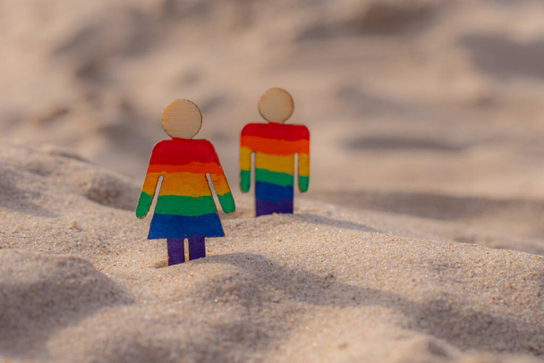 LGBT dřevěné lidi na pláži na písku. Pár stojící na pláži s duhovou vlajkou, rovná práva, symbol komunity LGBT. LGBT vlajka na písečné pláži. Koncept letního cestování. Symbol stejného pohlaví - Fotografie, Obrázek