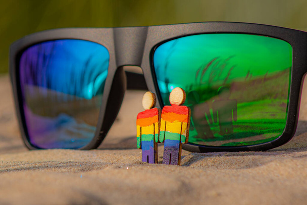 LGBT wooden people on the beach on the sand. Couple standing on beach with rainbow flag, equal rights, symbol of LGBT community. Sunglasses with LGBT flag on sandy beach. Summer travel concept. - Photo, Image