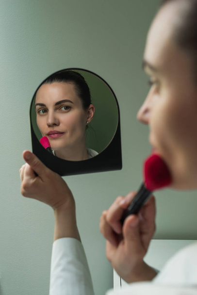 Europejska kobieta nakłada makijaż przed lustrem. Makijaż przed lustrem. Odbicie kobiety w lustrze. Piękno i samoopieka - Zdjęcie, obraz