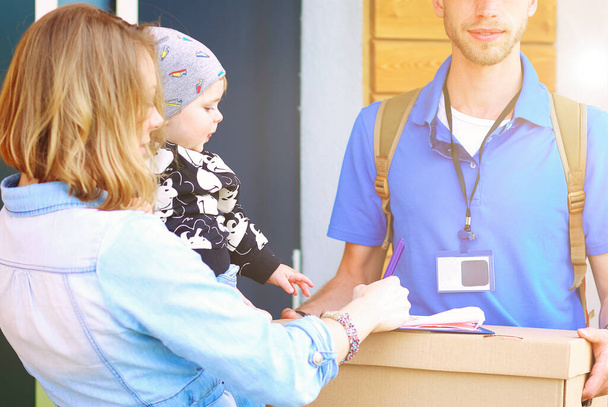 Smiling delivery man in blue uniform delivering parcel box to recipient - courier service concept. Smiling delivery man in blue uniform. - Foto, Bild