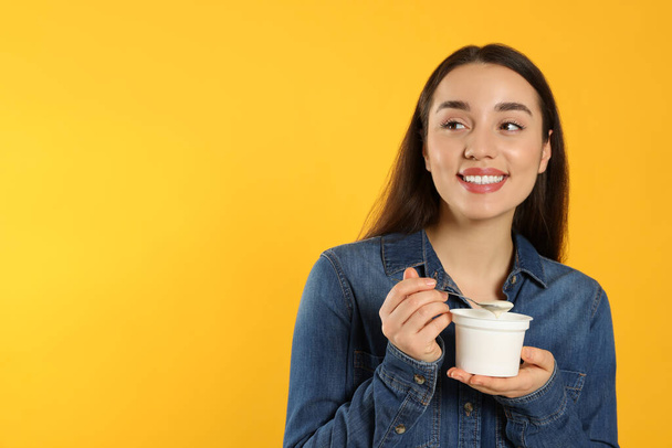 Happy woman with tasty yogurt on orange background. Space for text - Foto, afbeelding