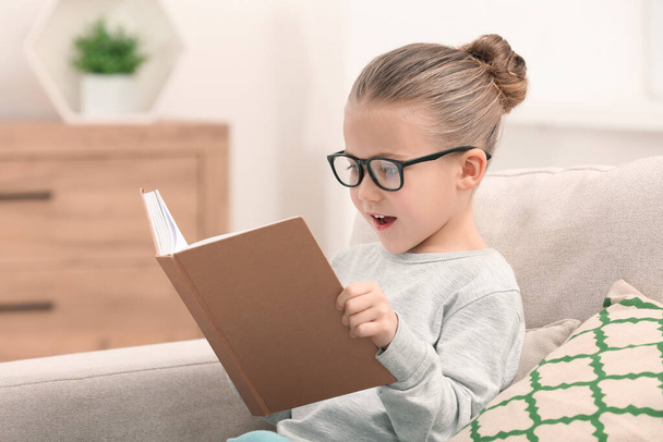 Portrait of cute little girl in glasses with book indoors - Fotografie, Obrázek