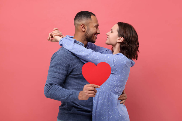 Lovely couple with paper heart on red background. Valentine's day celebration - Foto, afbeelding