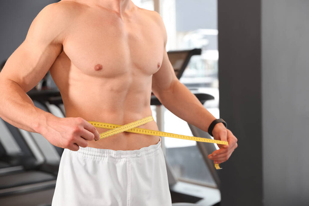 Athletic man measuring waist with tape in gym, closeup - Fotoğraf, Görsel