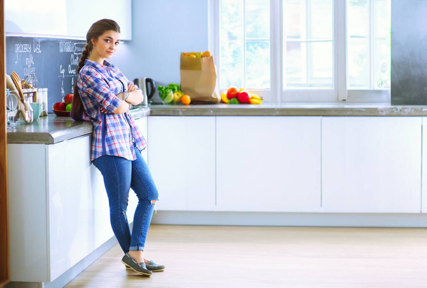 Retrato de mujer joven de pie con los brazos cruzados contra el fondo de la cocina - Foto, Imagen