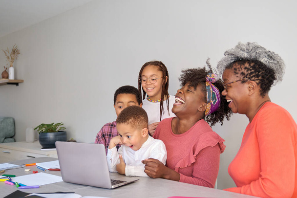 Boldog afrikai vízszintes kiterjesztett család néz laptop képernyőn, és nevet otthon. - Fotó, kép