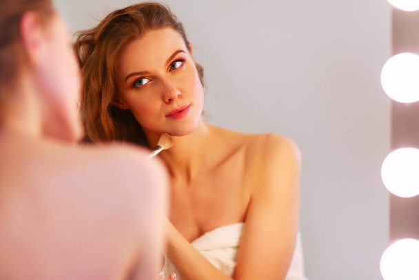 Young woman looking in the mirror and putting make-up on - Фото, зображення