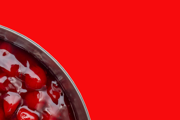 Cherry pie filling in a silver dish with a bright red background. One quarter of the dish showing . Clipping path, copy space - Valokuva, kuva