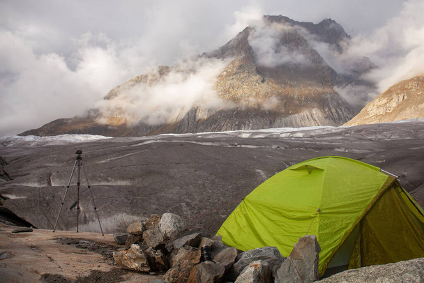 Tent and tripod on the background of a mountain in Swiss Alps. Aletsch Glacier. View of the Grieshorn. - Foto, imagen