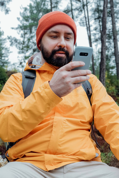 Homme barbu en chapeau utilisant un téléphone portable. Le gars qui regarde mobile et souriant.  - Photo, image